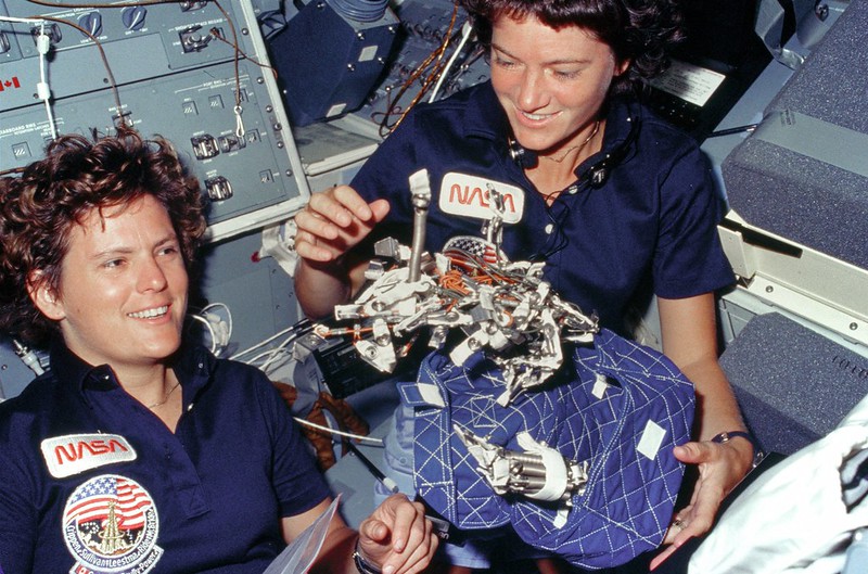 Two women in blue shirts holding a bag.